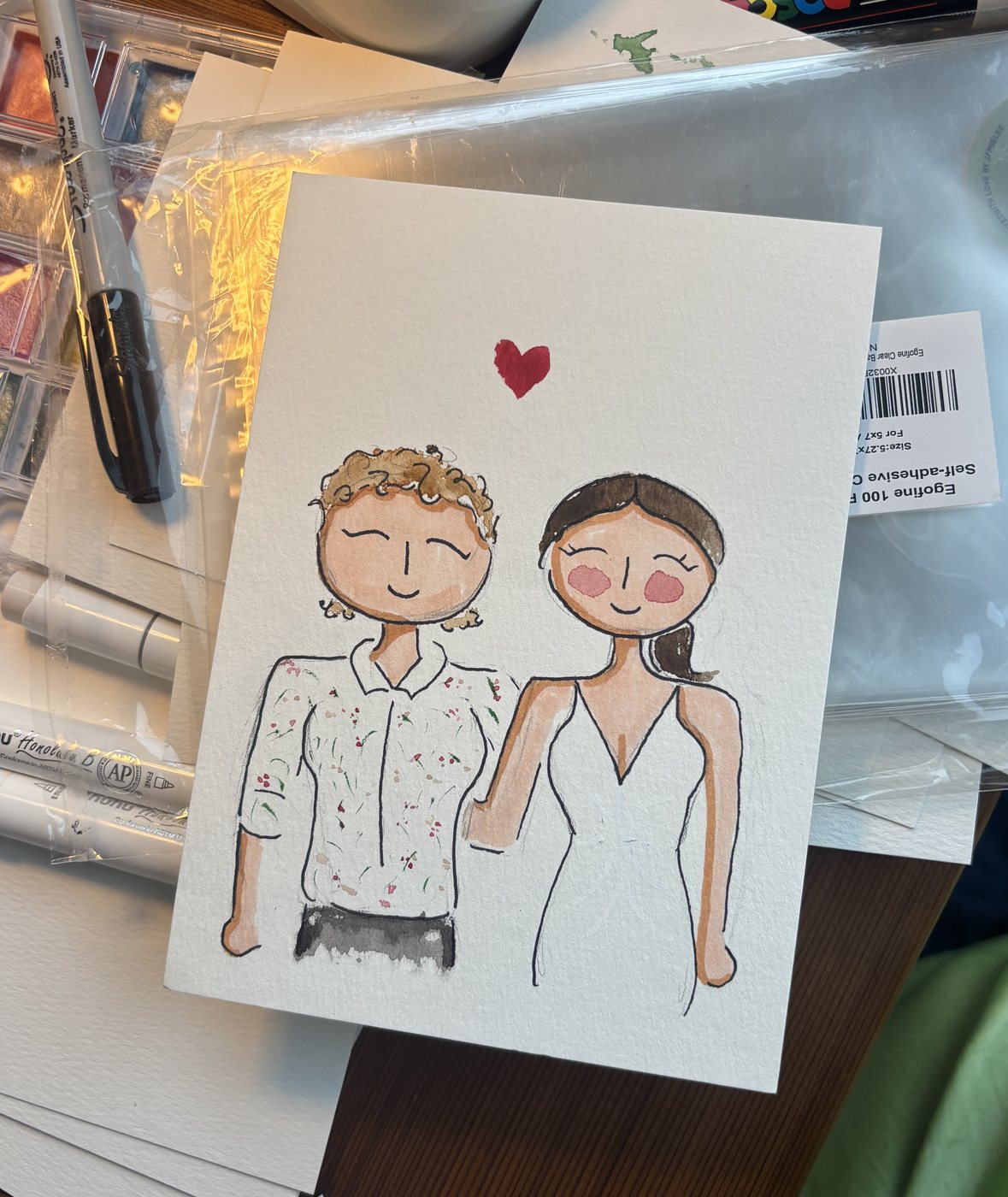 Live guest portrait of a couple holding hands, the woman in a white slip dress, with a red heart painted above them